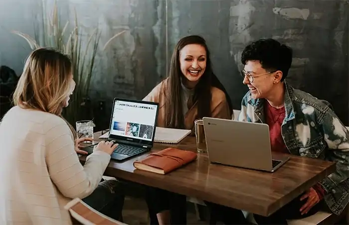 Three people engaged in a conversation, with two laptops in front of them, using DatumOffice’s Community module for social interactions